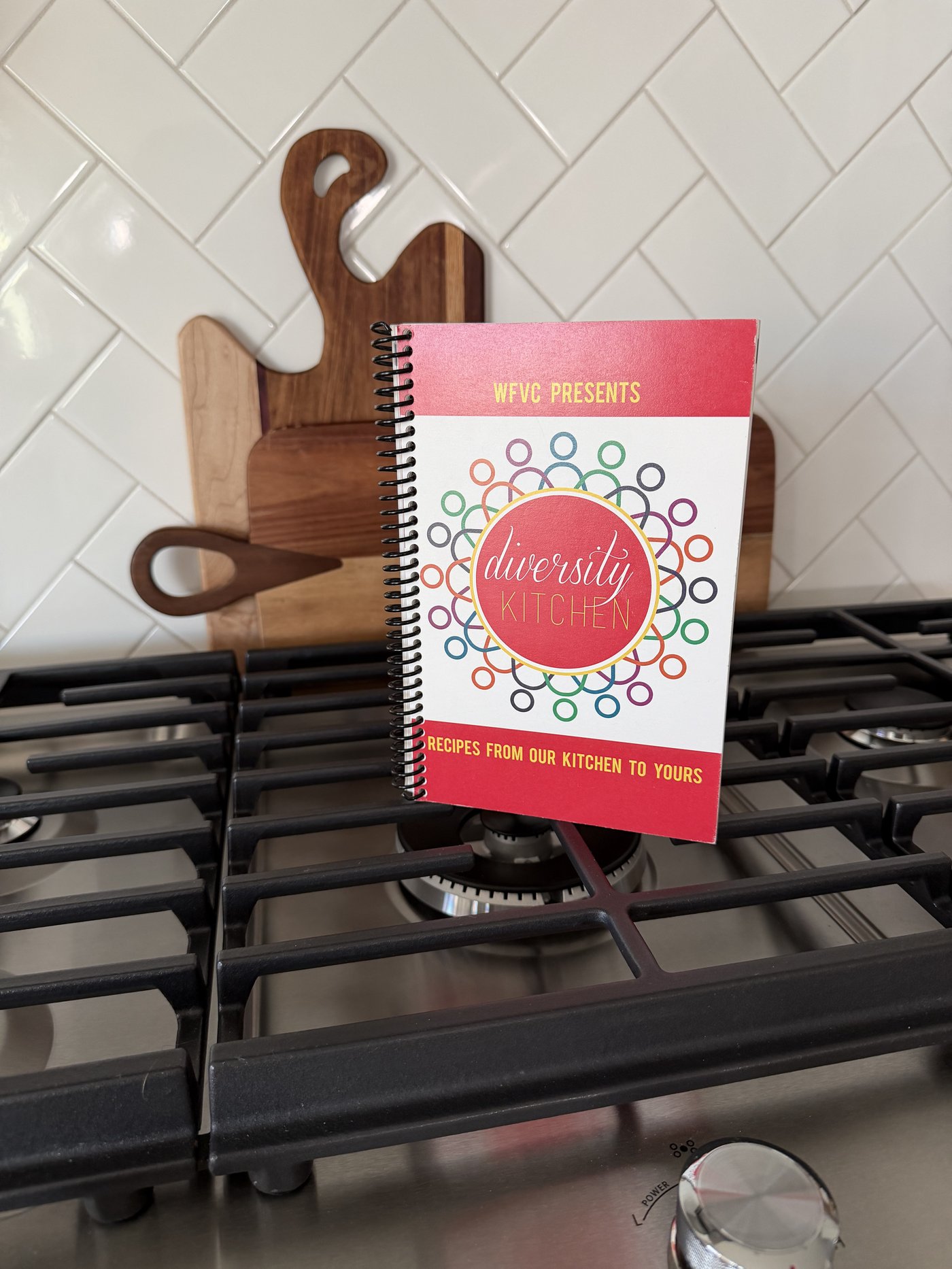 Diversity Kitchen cookbook cover, a spiral-bound book with a colorful ring pattern design